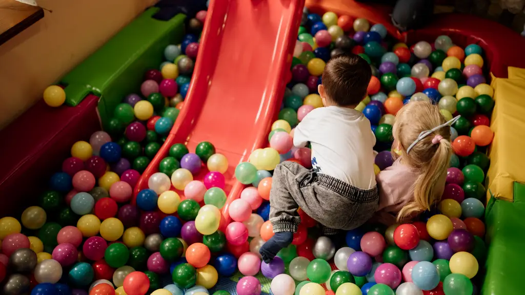 Two young children climbing beside a red slide in a colorful ball pit at an indoor play center